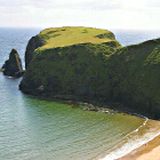 Grande scoglio coperto di verde che si riflette sul mare in estate